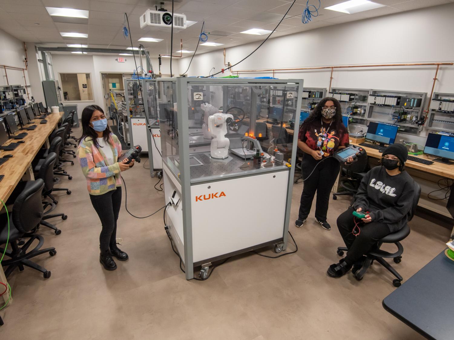 Three women students stand in a robotics and automation lab at Penn College.
