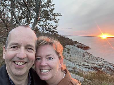 A photo of Frederik and Sonja Wenzel near the edge of a body of water with the sun setting in the background.