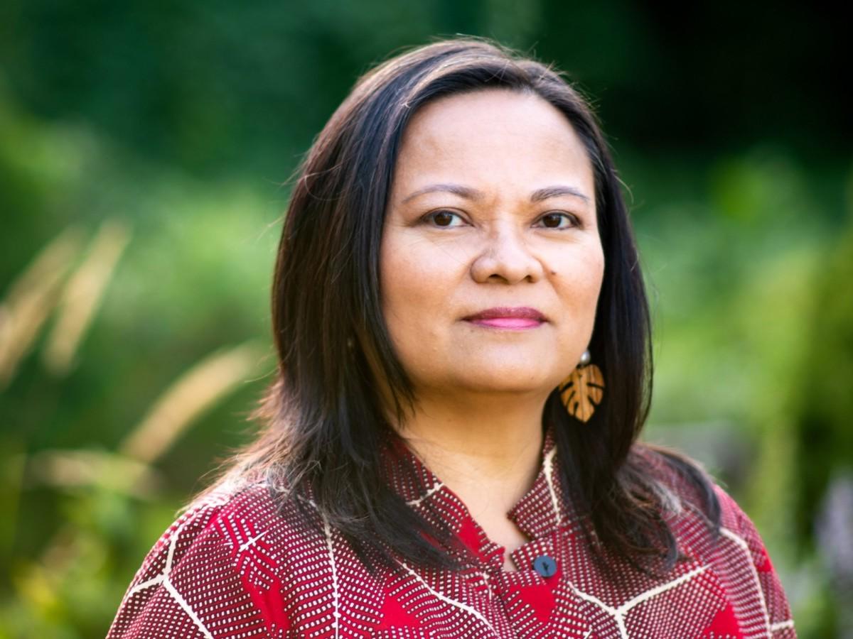 Grace Talusan wearing a red shirt standing outdoors against a green backdrop