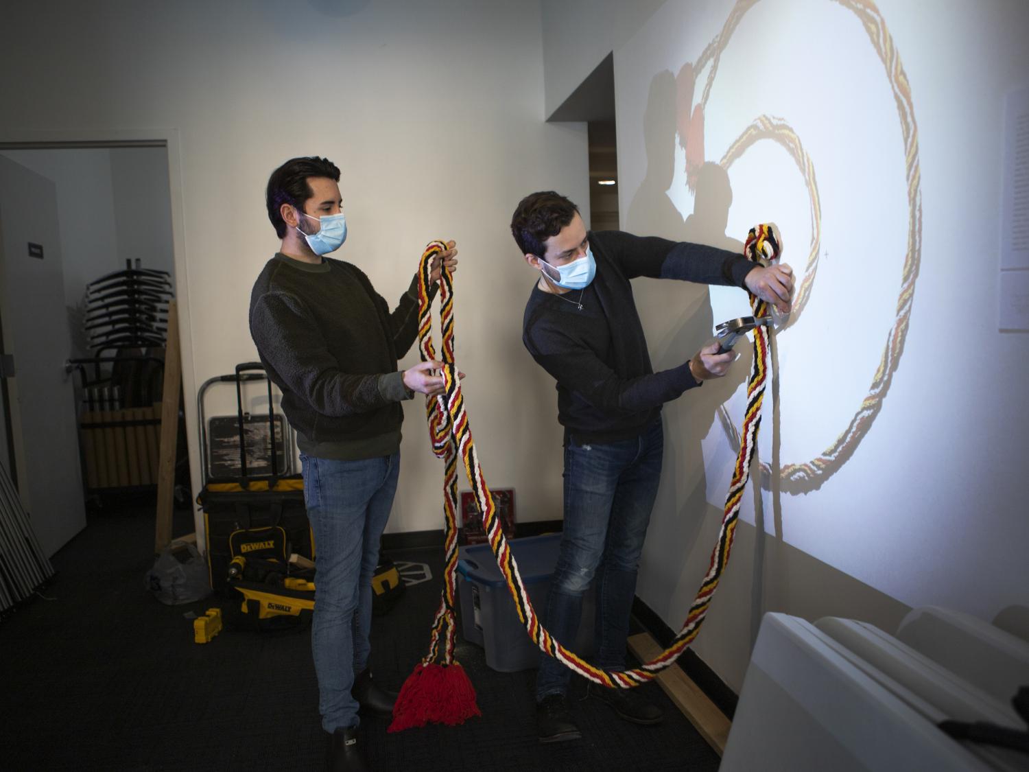 Two men attaching a colorful rope-like structure to a wall