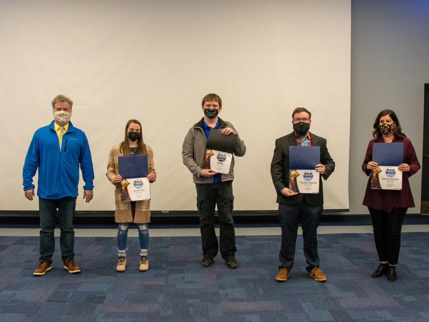 A group of five people standing in a row holding awards