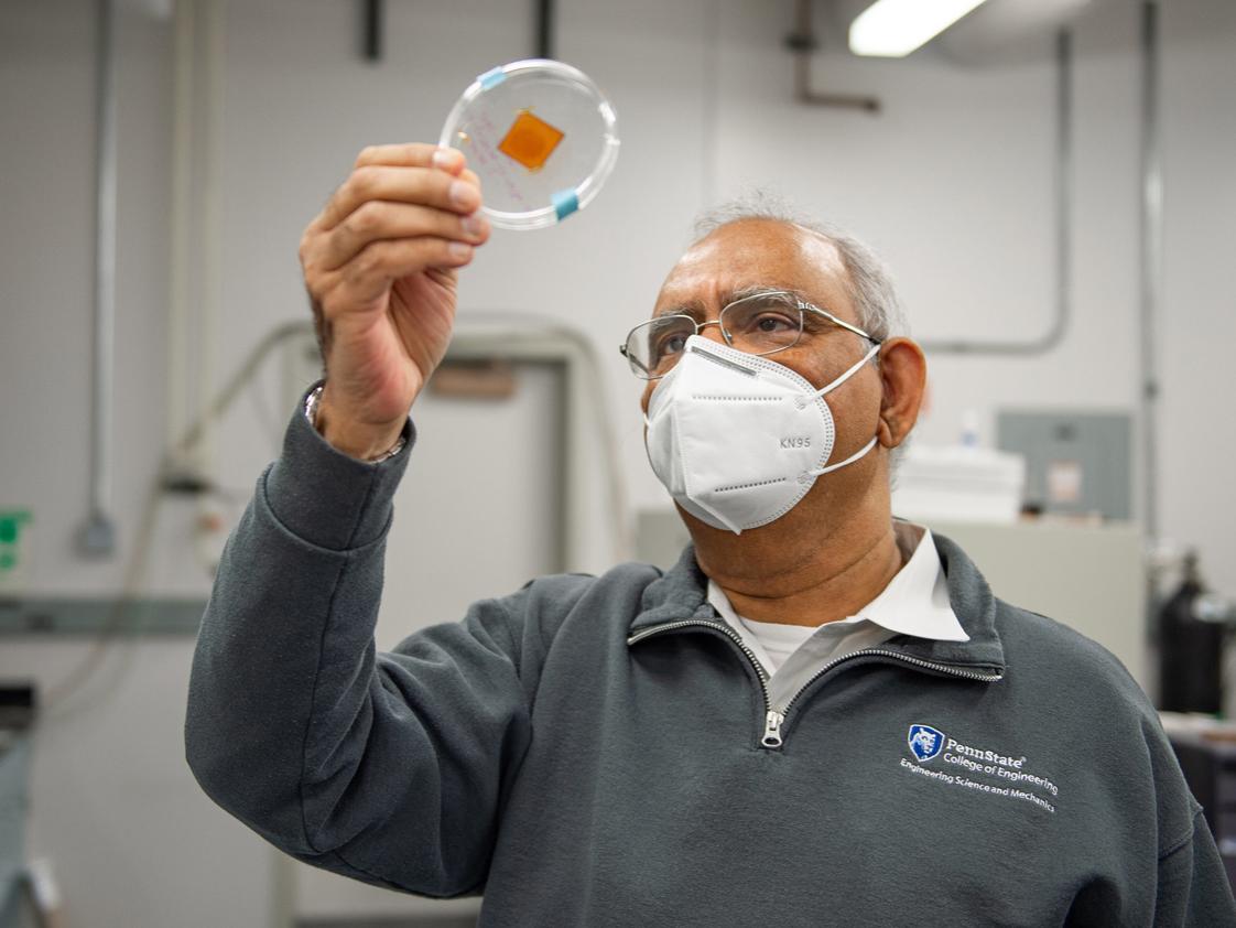 Researcher wearing glasses and a gray quarter-zip fleece holds up a petri dish containing a slip of tape with a fingerprint deposited on it