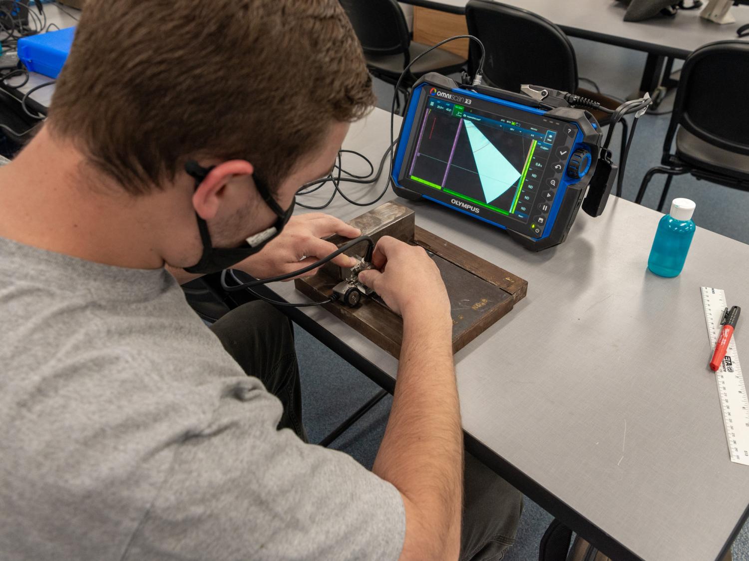 A student examines a welded plate with a machine