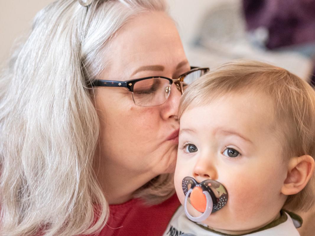 Woman leans over and kisses her infant grandson.