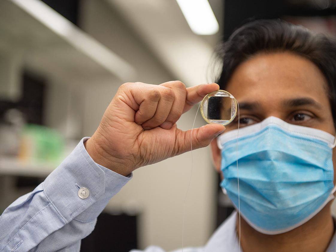 A man holds up and stares at a small glass plate.