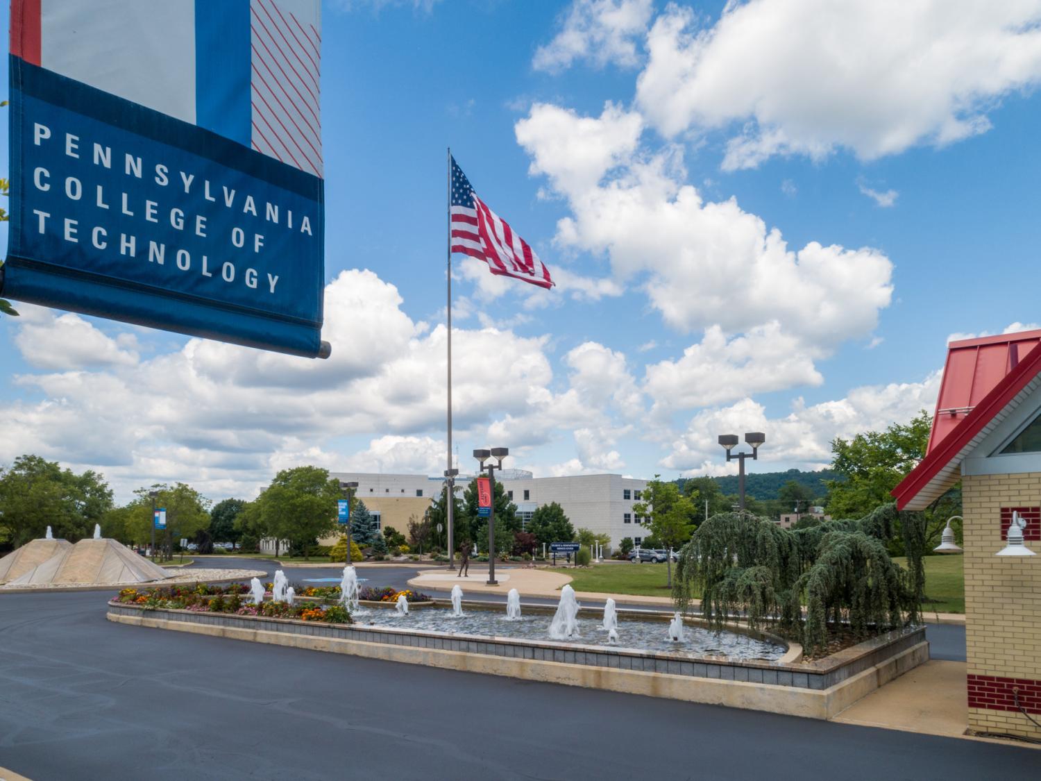 A sign that says "Pennsylvania College of Technology" on the Penn College campus with blue skies and the American flag behind it.