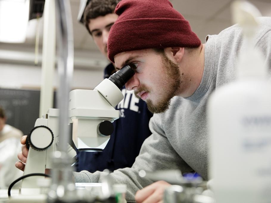 A student looking through a microscope in a classroom.