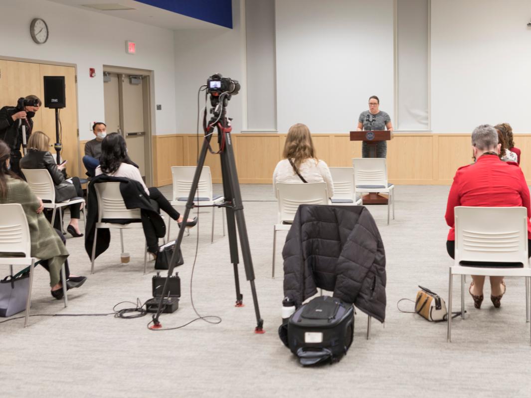 A woman speaks at a podium while people sit in front of her and listen
