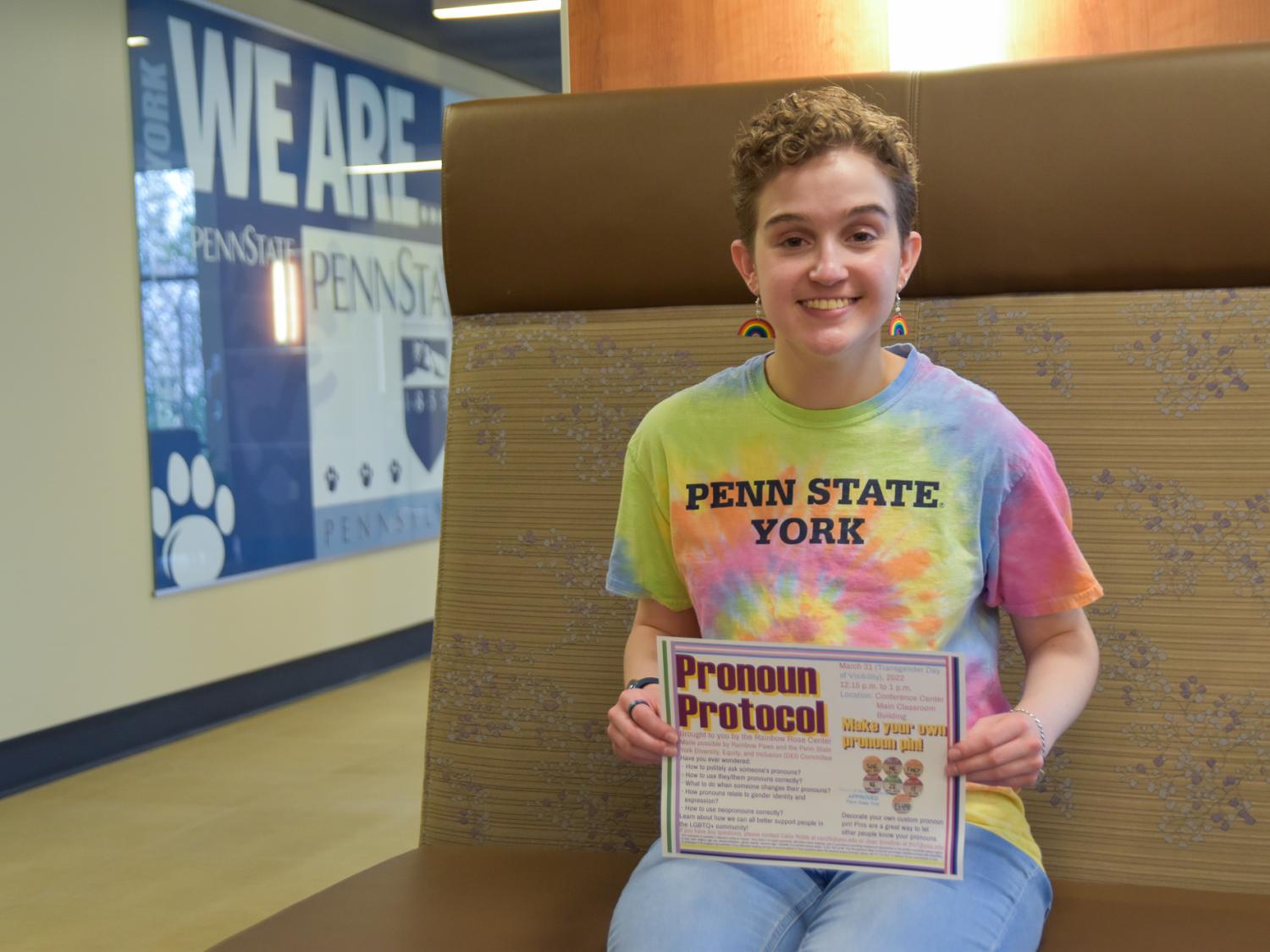 Seated short-haired female wearing colorful shirt hold program sign for Pronoun Protocol program