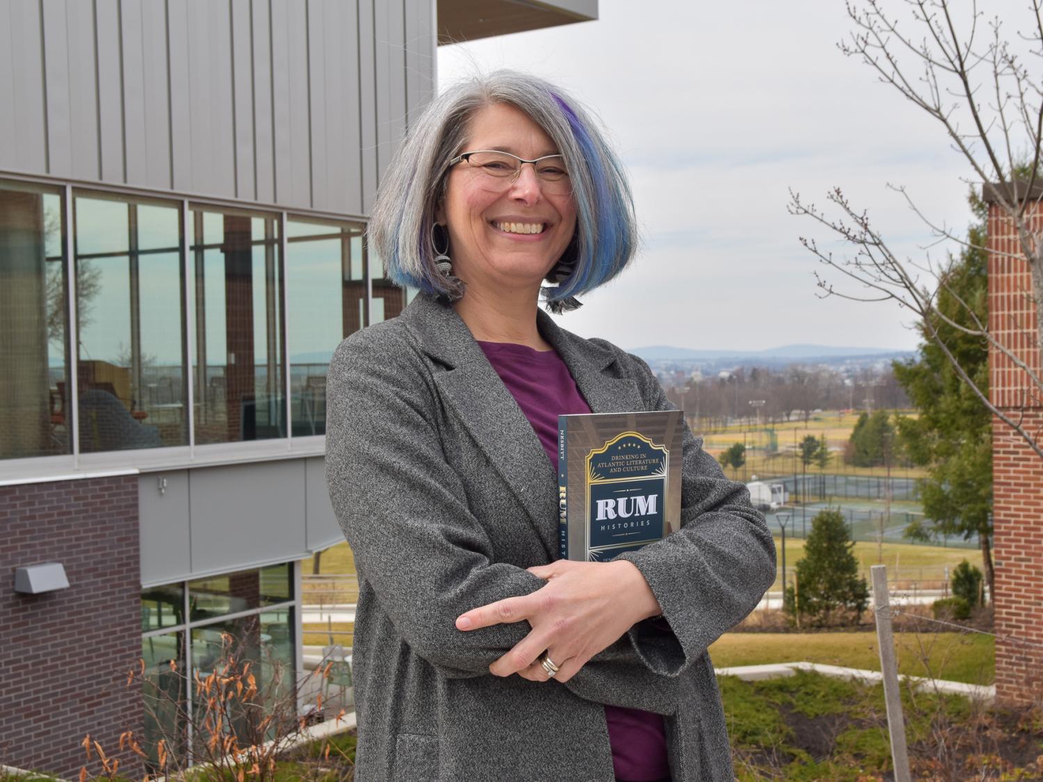 Female English faculty member holding her recently published book standing outside at Penn State York