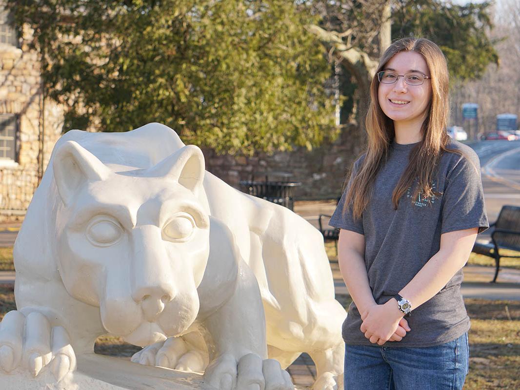 Female student standing outdoors next to Nittany Lion statue.