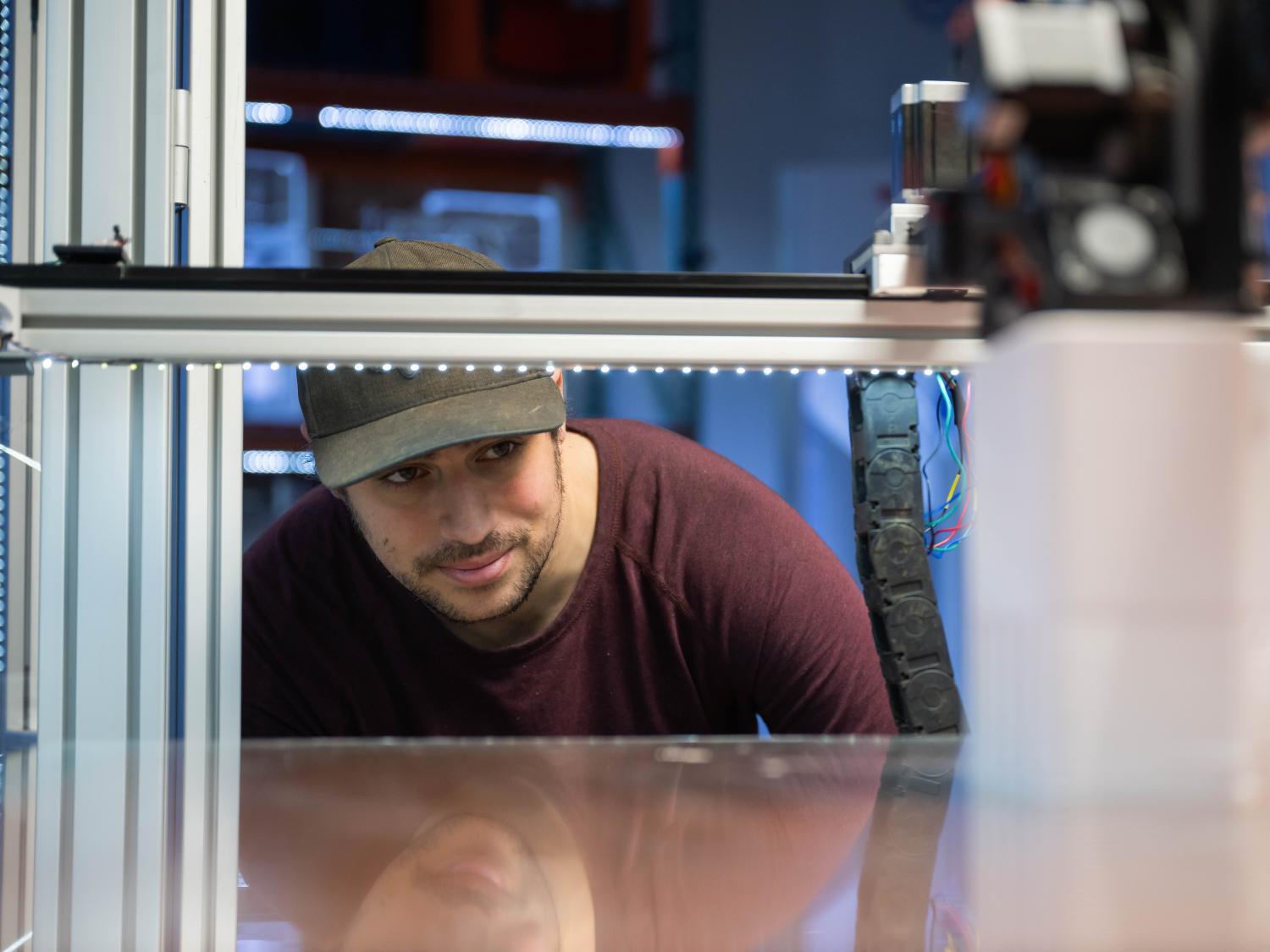 A Penn State Behrend student ducks down to look into a large-scale 3D printer.