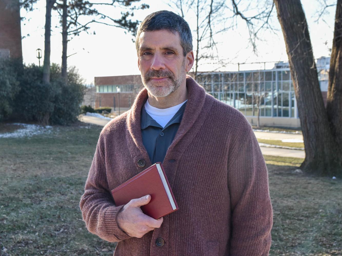 Bearded male standing outside holding abook
