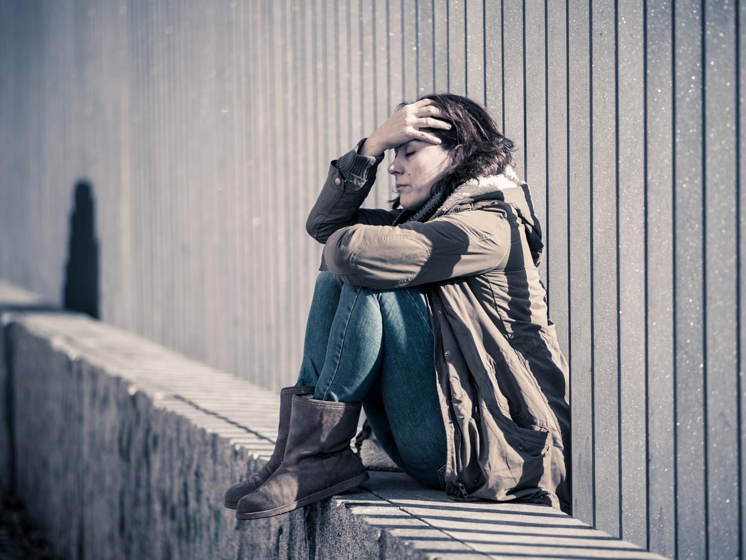 A woman sitting on a stone ledge with her knees pulled up and head in her hands
