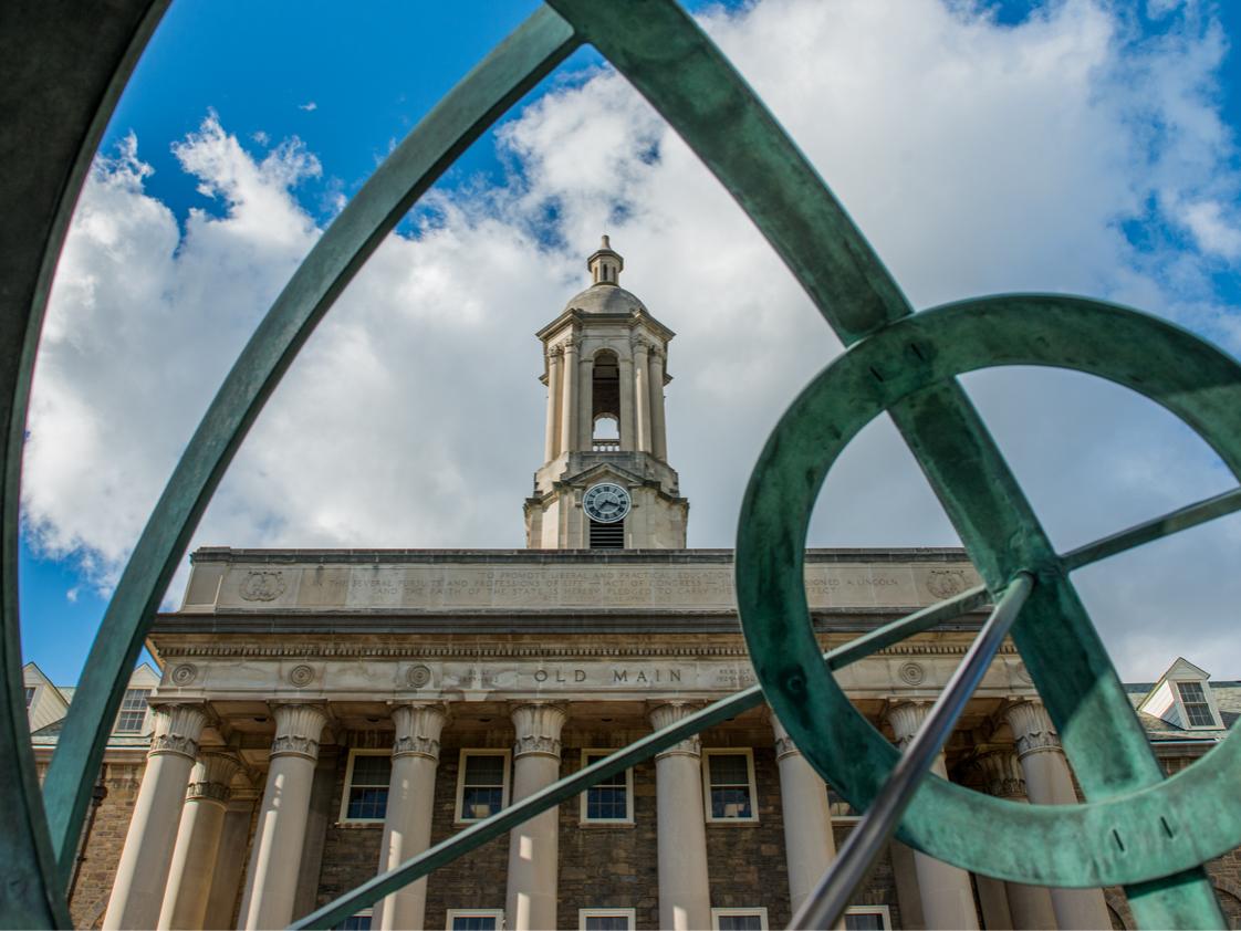 Penn State's historic Old Main building and bell tower are seen on a partly cloudy day.