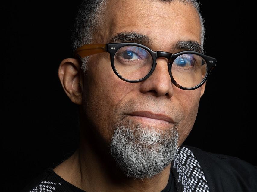 Headshot of a black man with a grey goatee wearing dark colored, round glasses