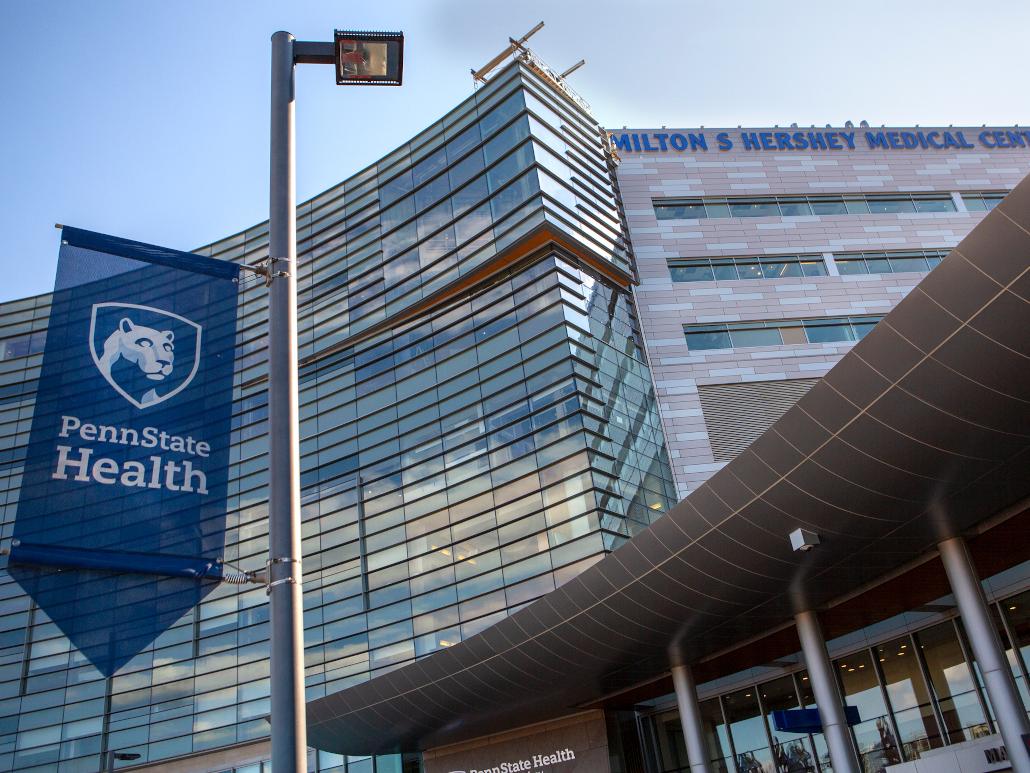The front of a hospital with a banner in the foreground that says, "Penn State Health"