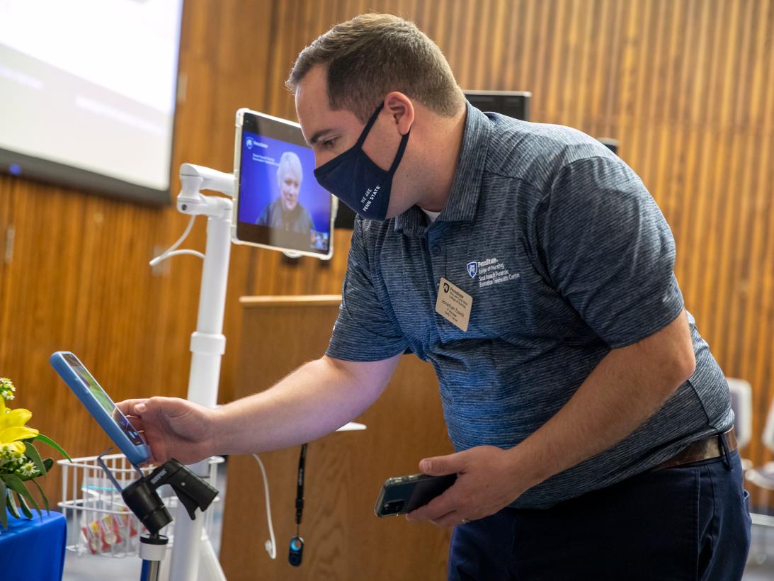 A man leans over a smart phone, demonstrating how it will be used to connect to experts via telehealth