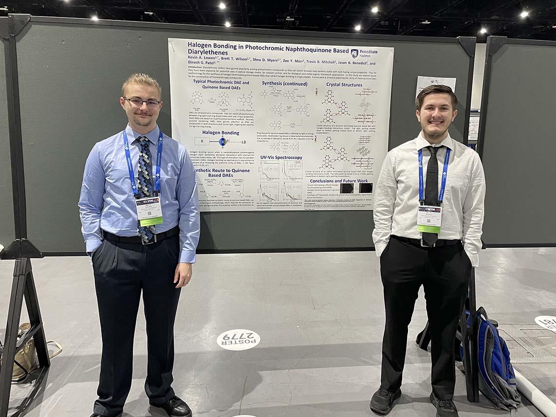 Two students standing in front of a white poster board.