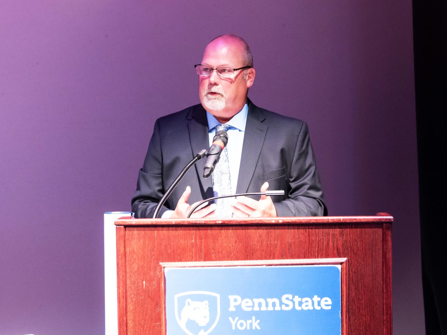 Male person professionally dressed who is speaking at a Penn State York podium. 