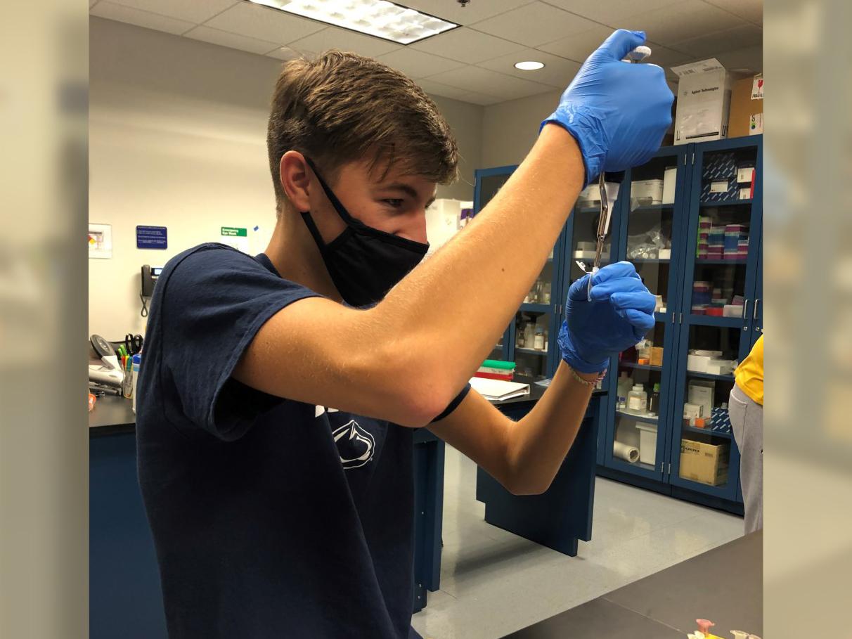 Male student wearing a facemask and working in a lab setting on undergraduate research.