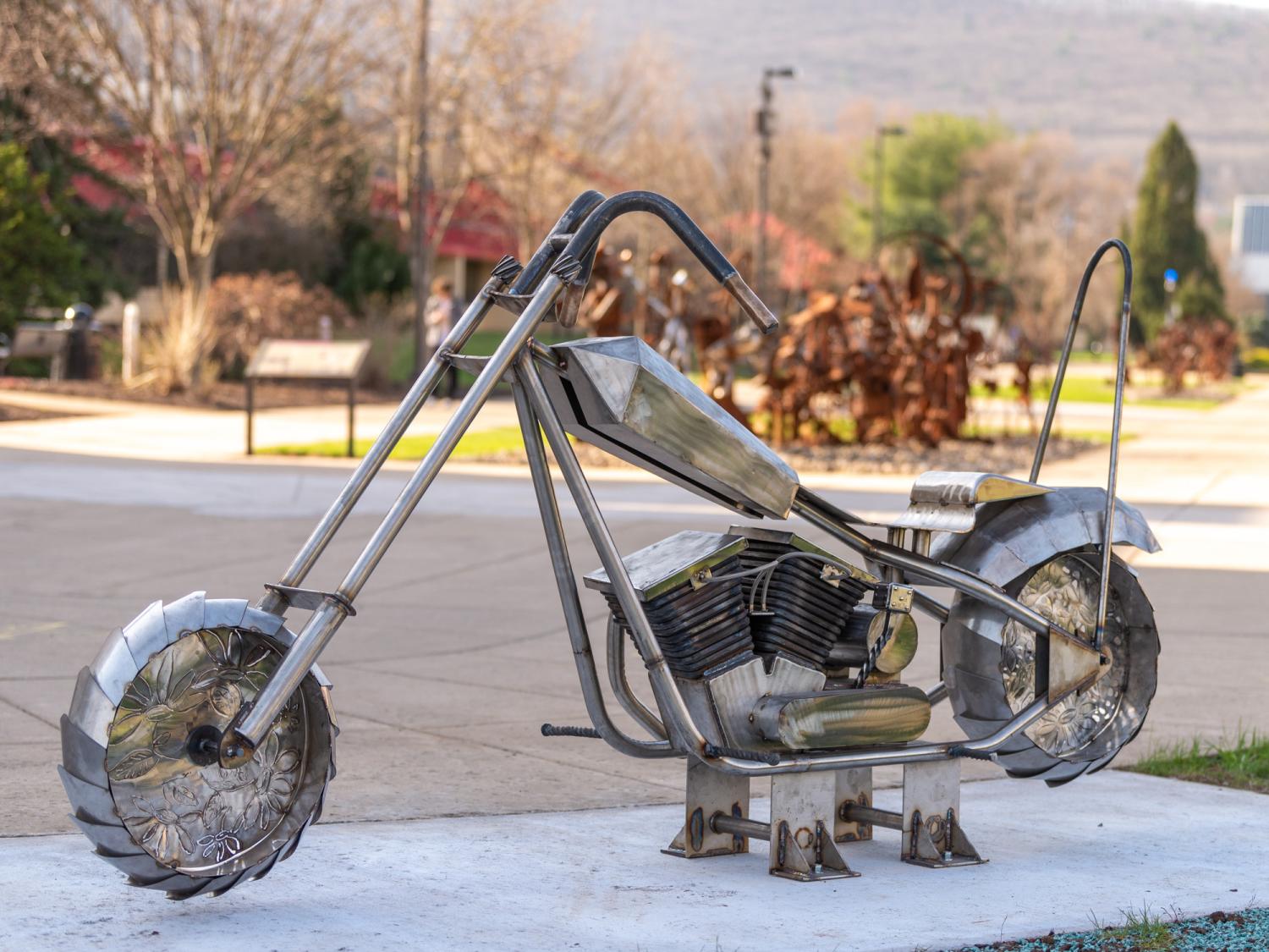 A sculpture of a stainless steel motorcycle outside on a platform