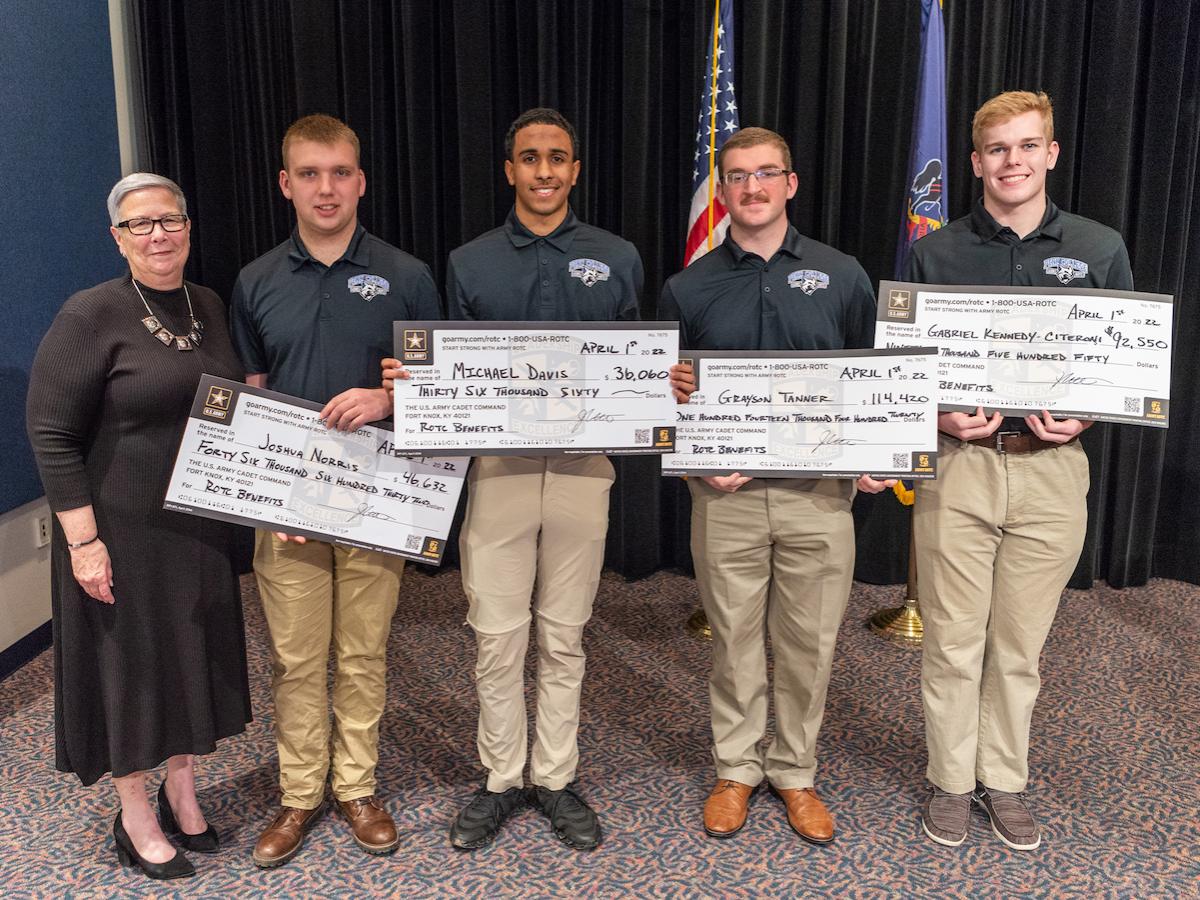 Penn College President Davie Jane Gilmour joins four ROTC cadets holding large checks showing the amounts of their Army ROTC benefits