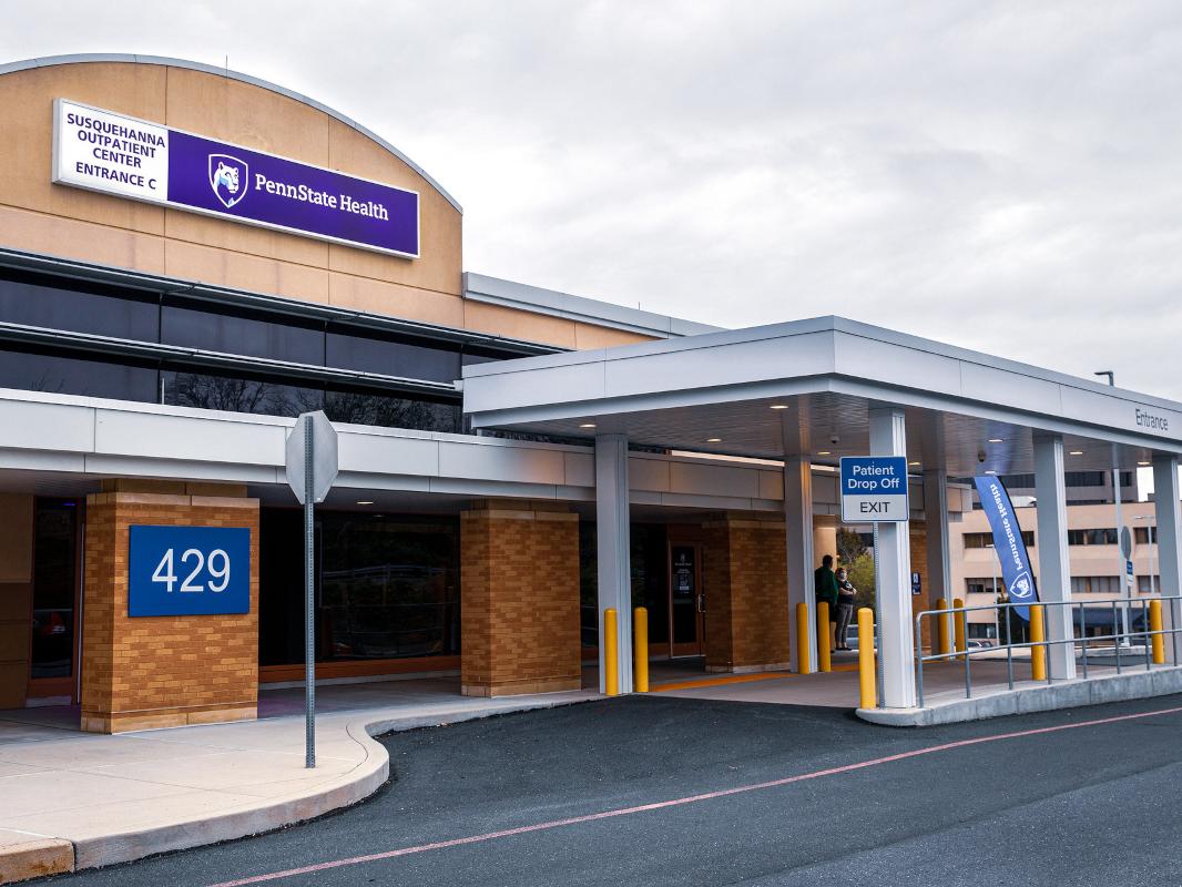 An external photo of the Penn State Health Specialty Services building, the exterior of which is built with brick, glass and other materials. A covered drive-through entrance labeled "Patient Drop Off" is in front.