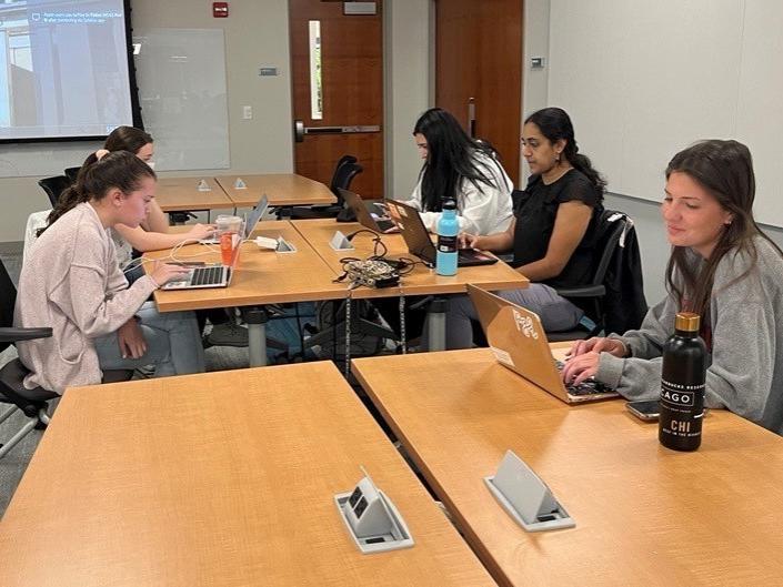 A group of five female students work on their individual laptops to update a Wikipedia page