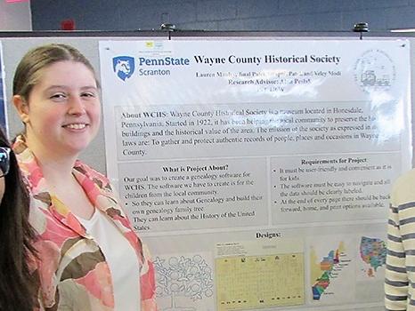 three students stand next to their research poster at a past fair event