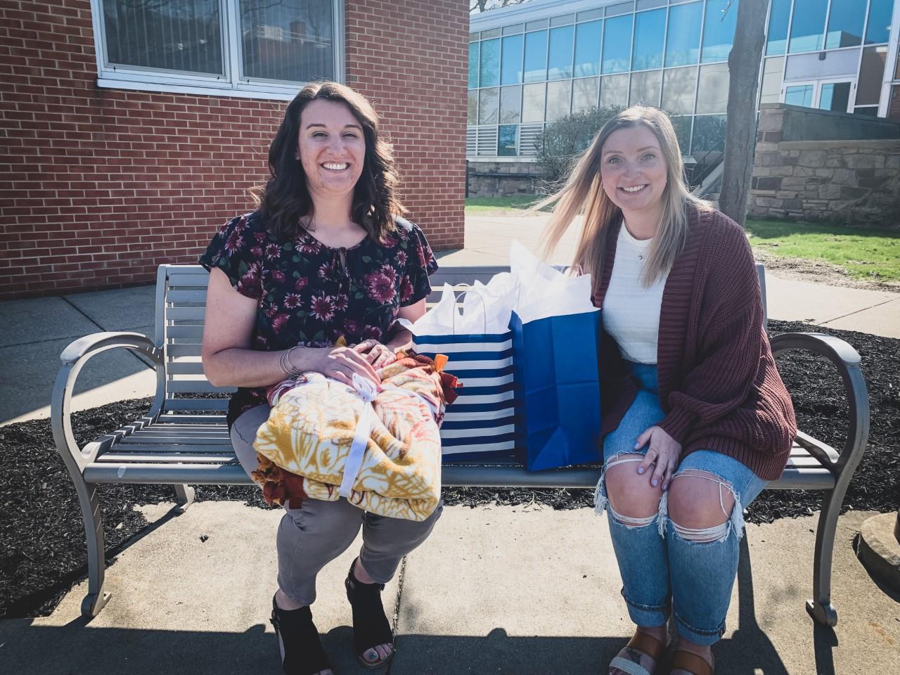 two women sit on a bench exchanging gifts