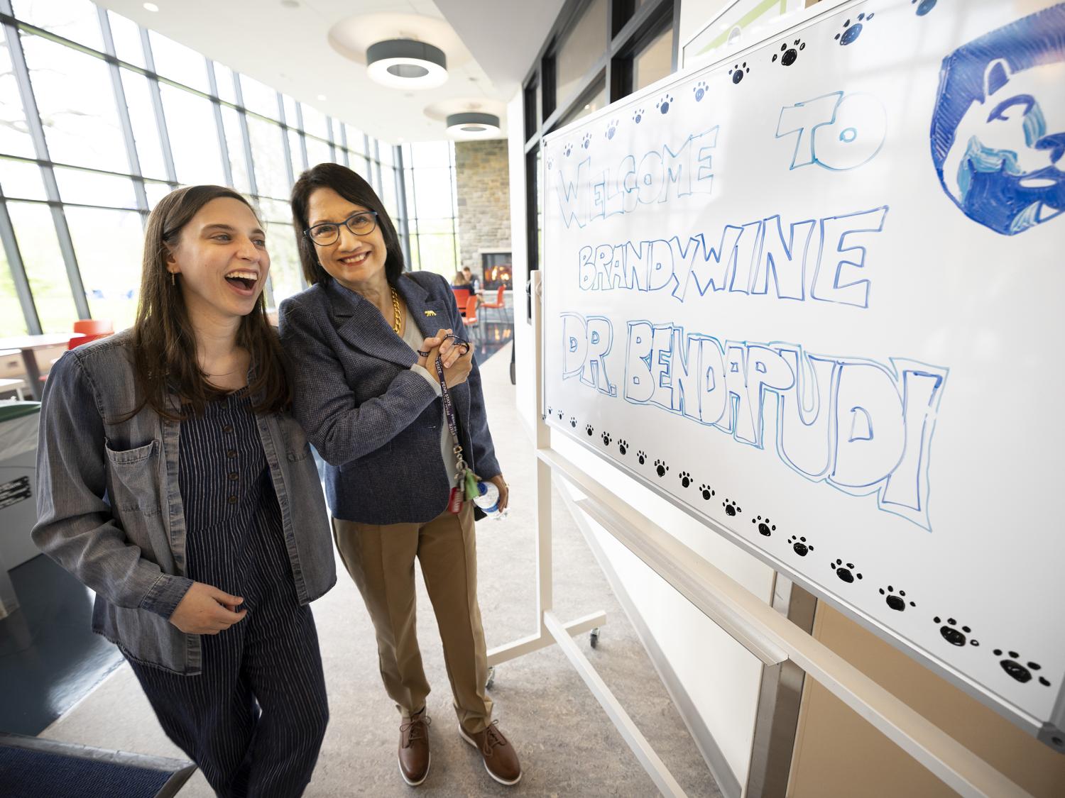 Two women stand next to a white board with a welcome message.