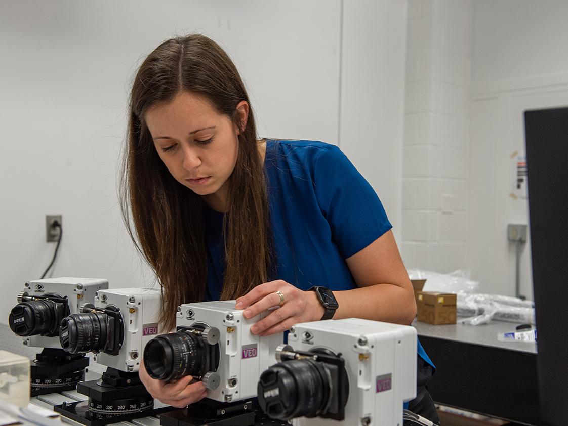 A woman adjusts a stationary camera lens. 