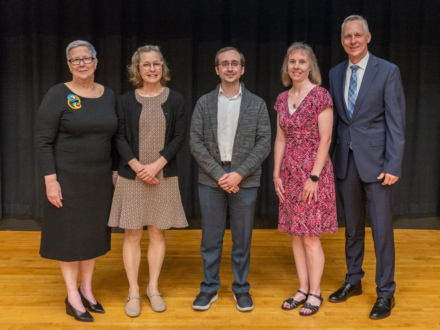 A group of five people stand in a row for a photograph.