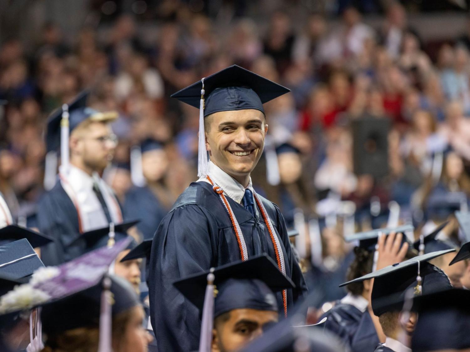 A graduate stands and smiles during Penn State Behrend's spring commencement ceremony.