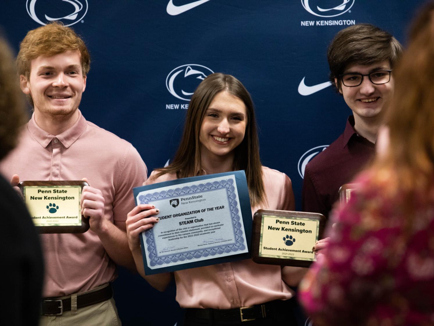 Three students smile to take photo while holding awards