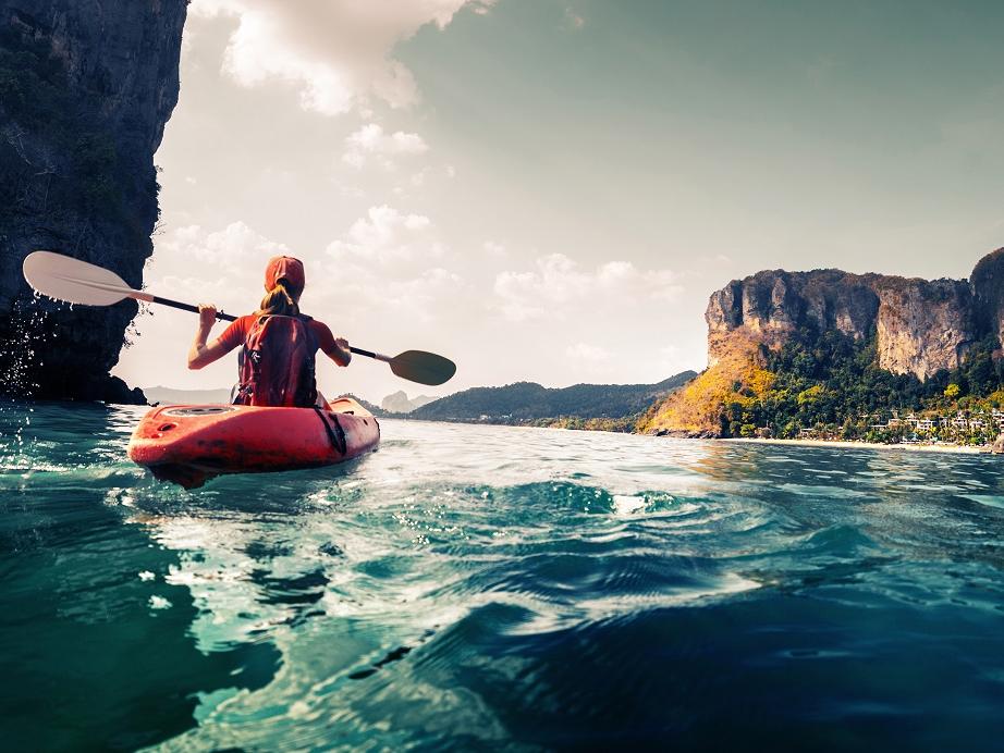 A woman paddles a kayak in a calm, tropical bay.