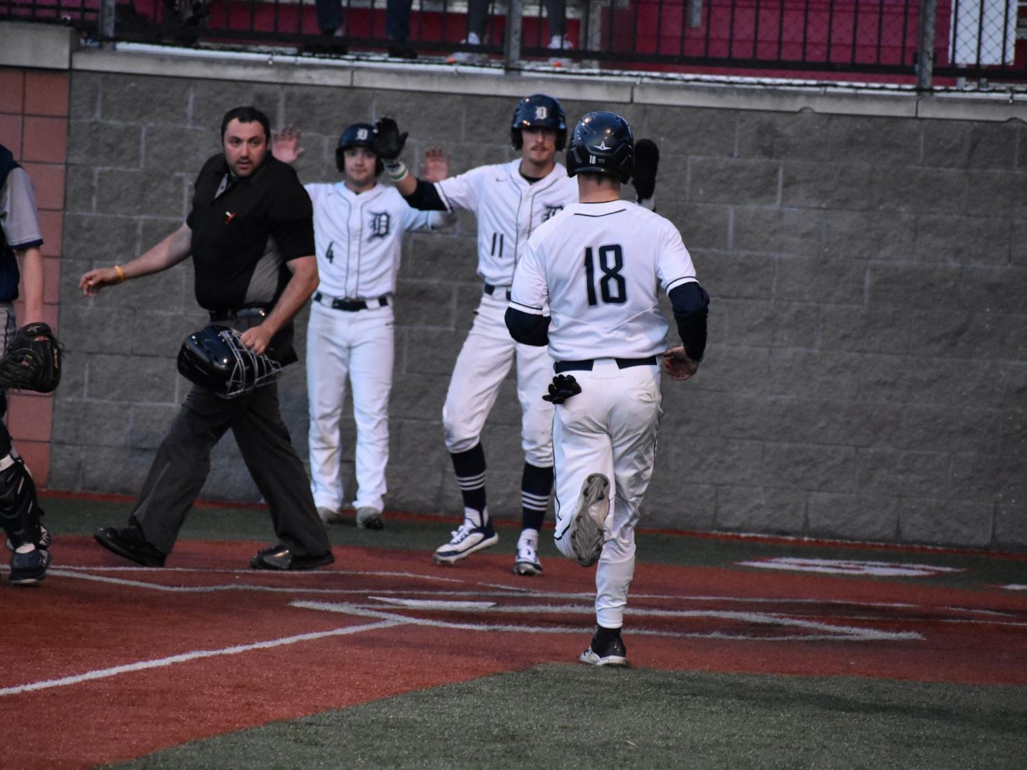 Baseball players welcome teammates at home plate after scoring