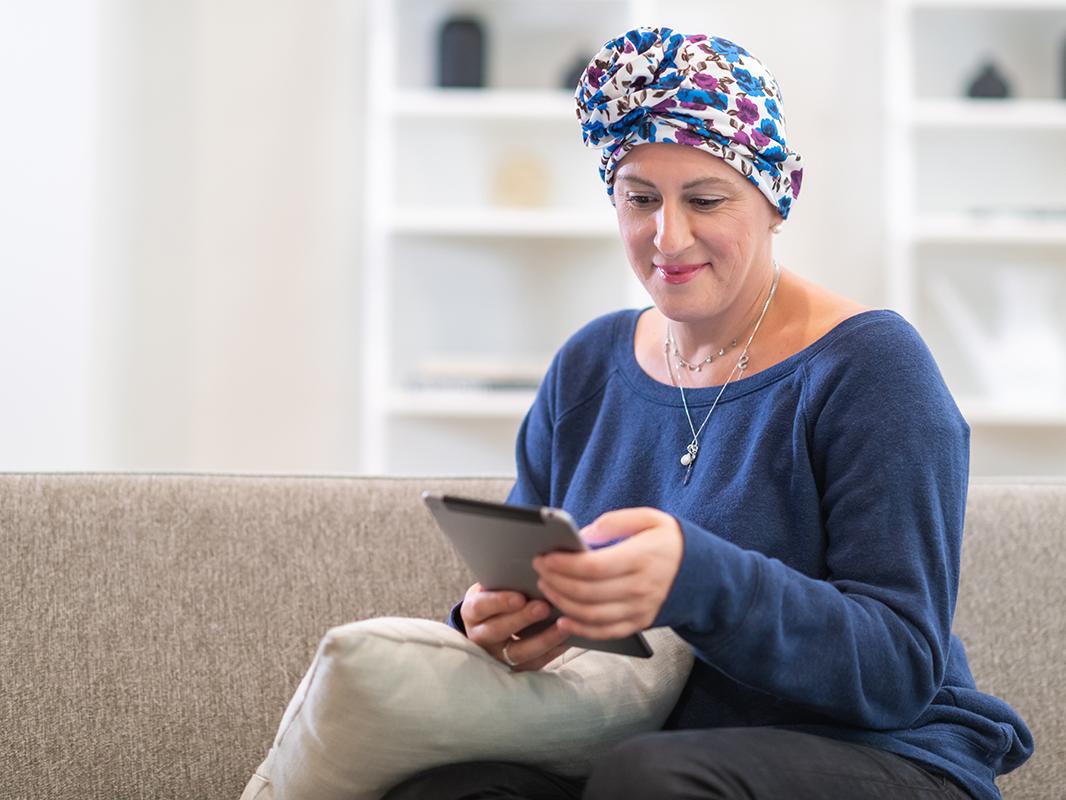 A female cancer patient uses a tablet while sitting on a couch.