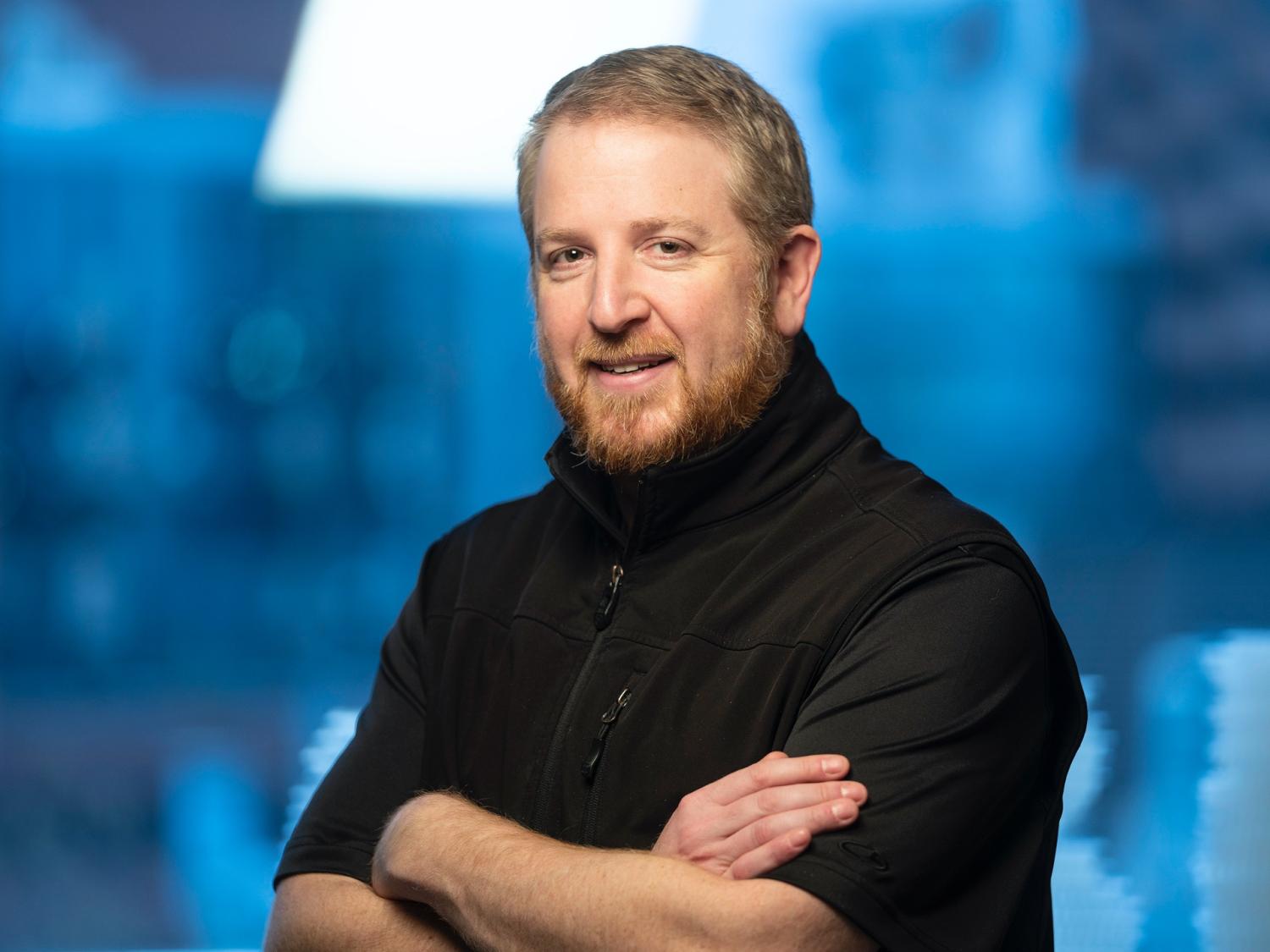 A man stands with his arms crossed looking at the camera with a smile. 