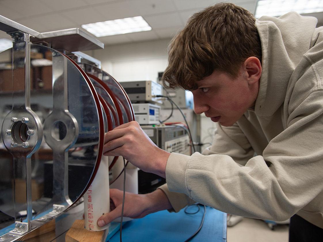 A person adjusts a wire on a metal disc. 