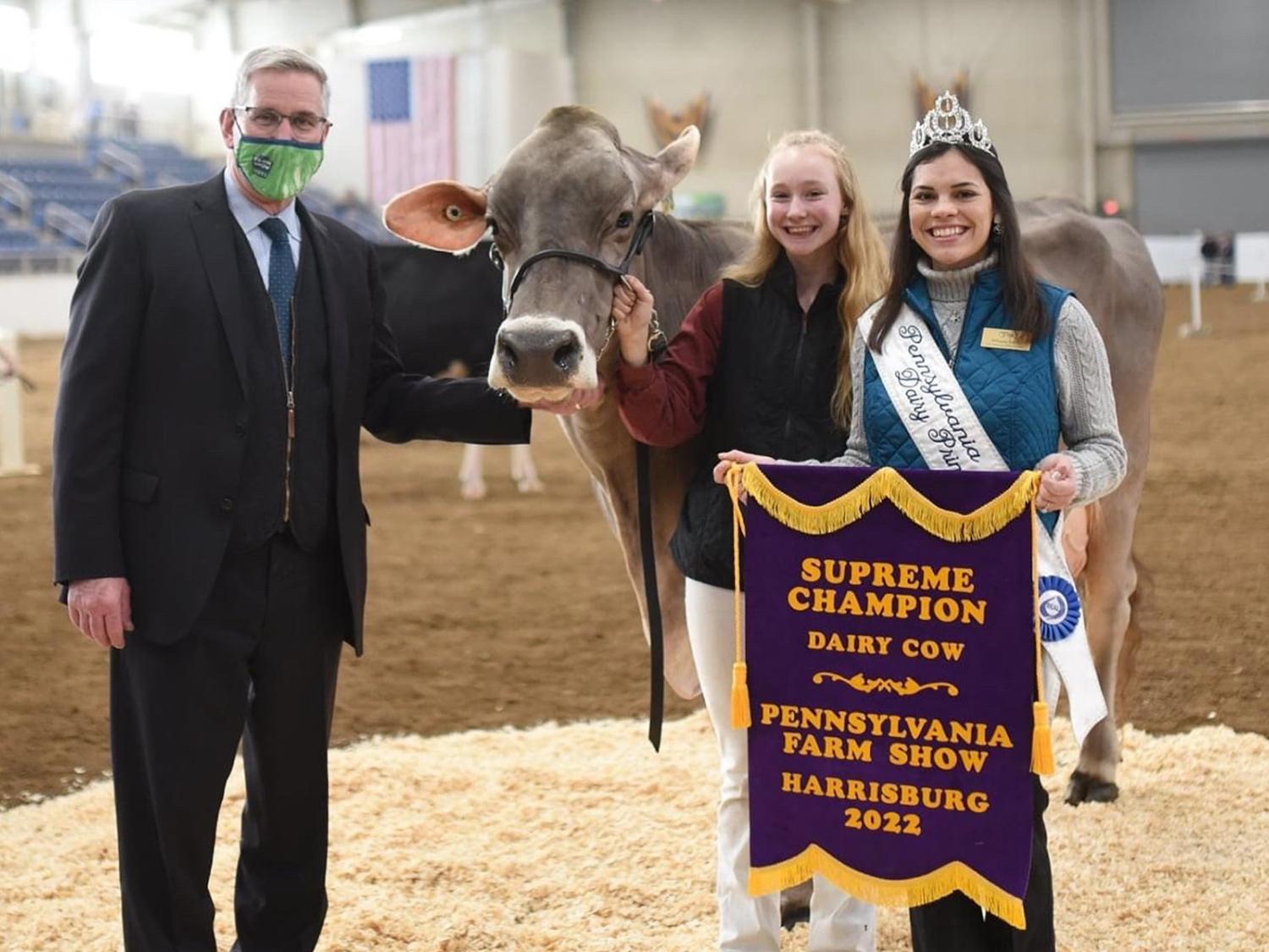 Mikayla Davis stands in a show ring next to two other people and a dairy cow while holding a banner.