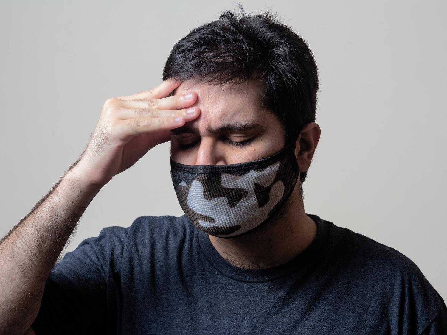Man wearing a medical face mask wincing and gripping his forehead