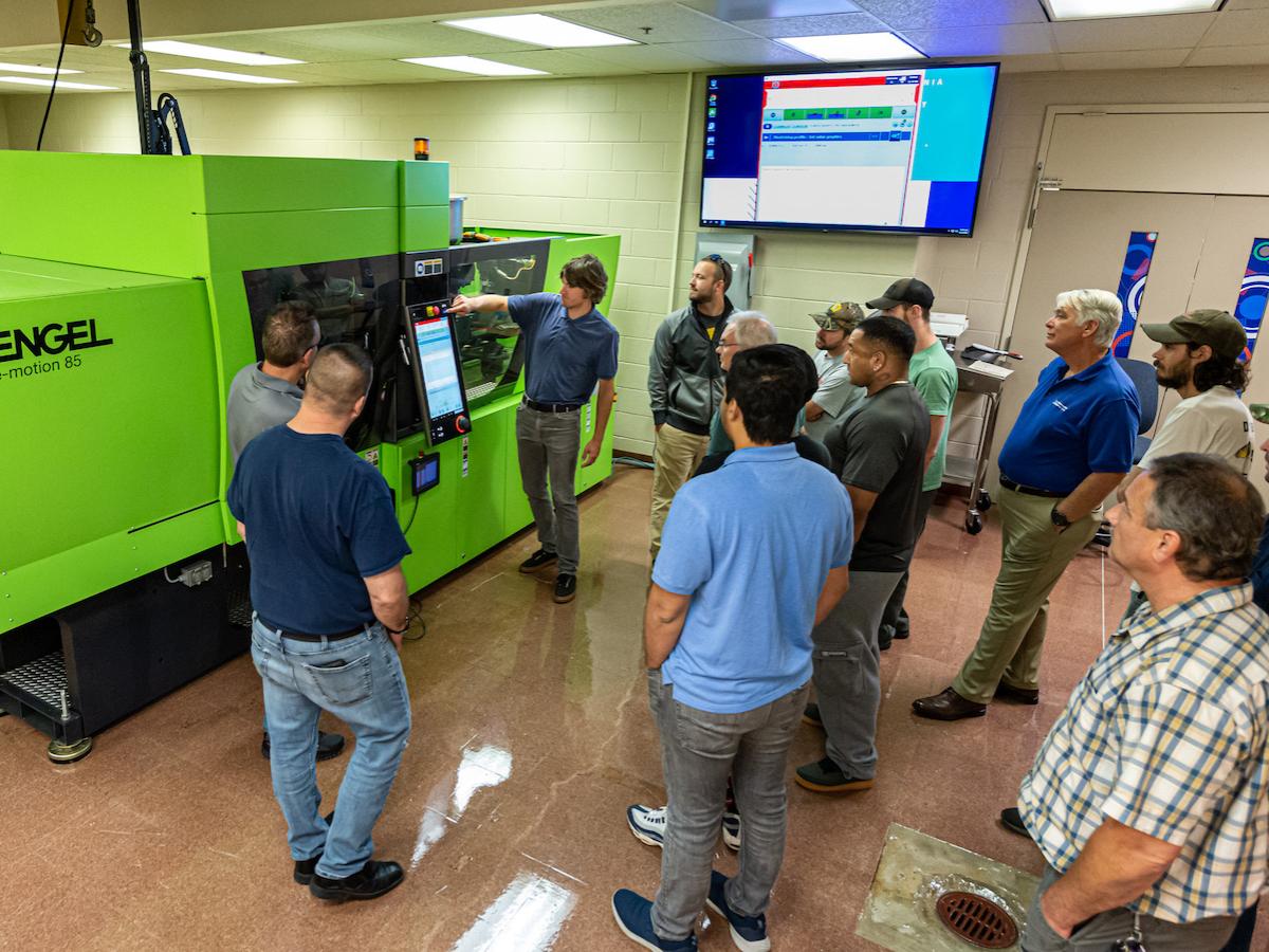 A group of people gather around a lime-green-colored all-electric injection molding machine in a Penn College lab.