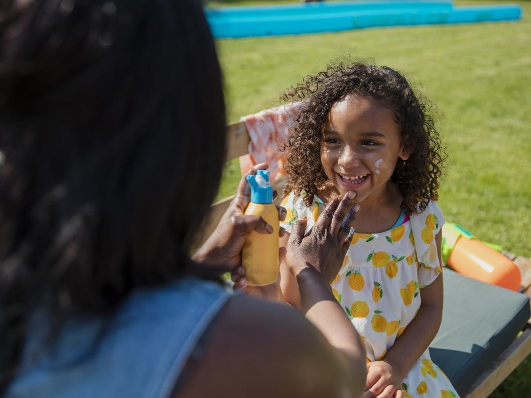 Over the shoulder view of a mother putting sunscreen on her daughter. They are in a garden in summer.