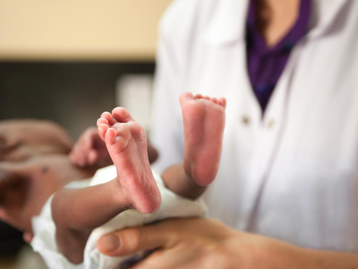 Photo of a doctor holding a newborn baby in a diaper, with the photo focusing on a close up of the baby’s feet. 