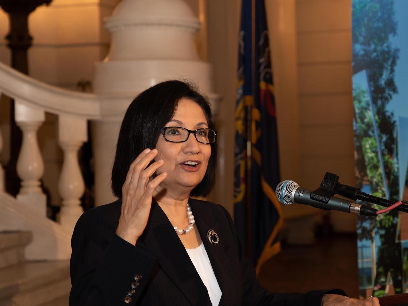 Penn State President Neeli Bendapudi speaks at a podium in the rotunda at the state Capitol
