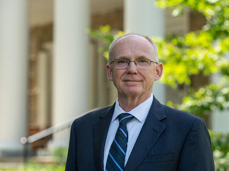 Anthony Atchley stands outdoors with greenery and building in background.