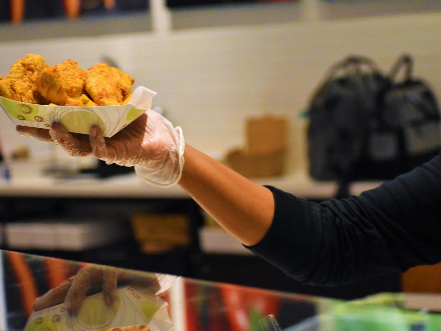 A gloved hand holds a container of fried food over a counter