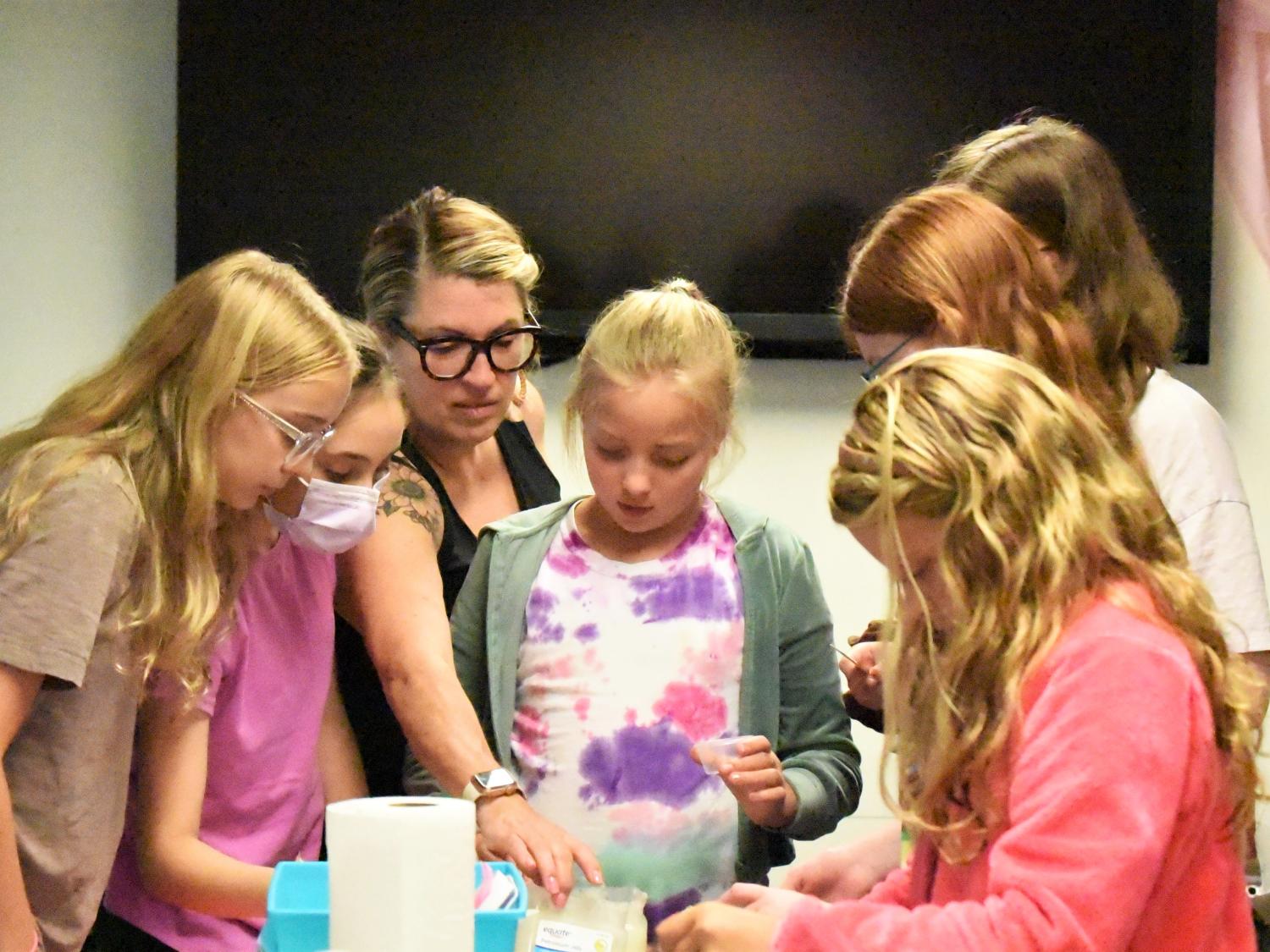 A group of girls gather around a craft table as they make their own lip balms and body sprays.